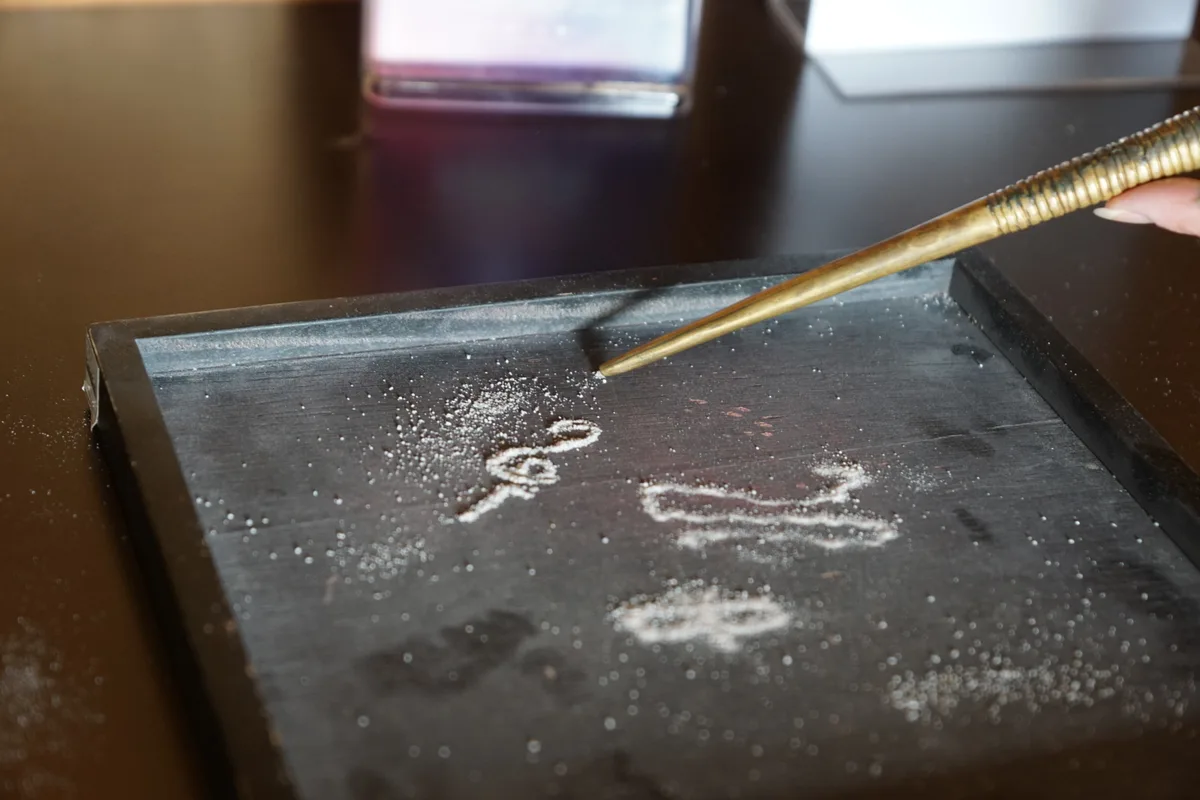 Man sieht etwas Sand aus der Spitze eines Metallrohres rieseln.