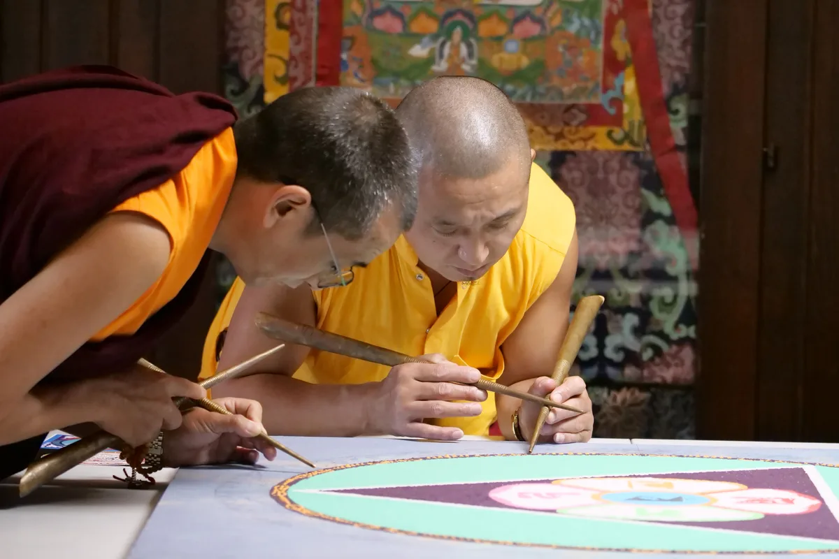 Zwei Mönche zeichnen ein Sandmandala.