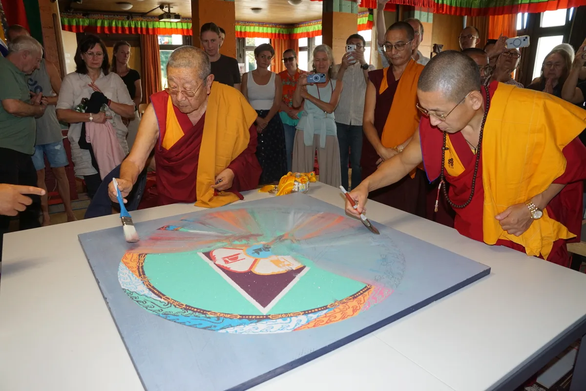 Man sieht buddhistische Mönche, die mit Pinseln ein Mandala aus Sand zusammenwischen.