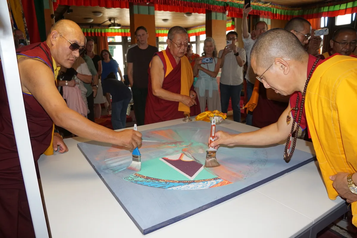 Man sieht buddhistische Mönche, die mit Pinseln ein Mandala aus Sand zusammenwischen.