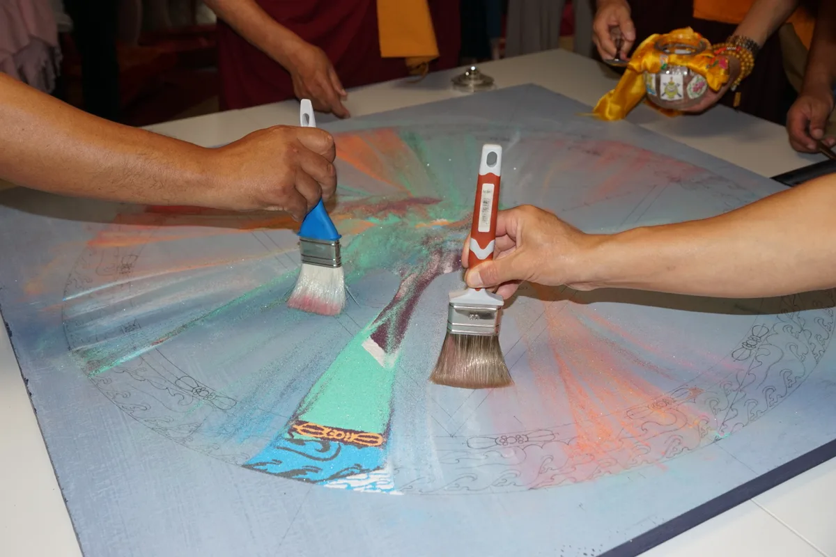 Man sieht buddhistische Mönche, die mit Pinseln ein Mandala aus Sand zusammenwischen.