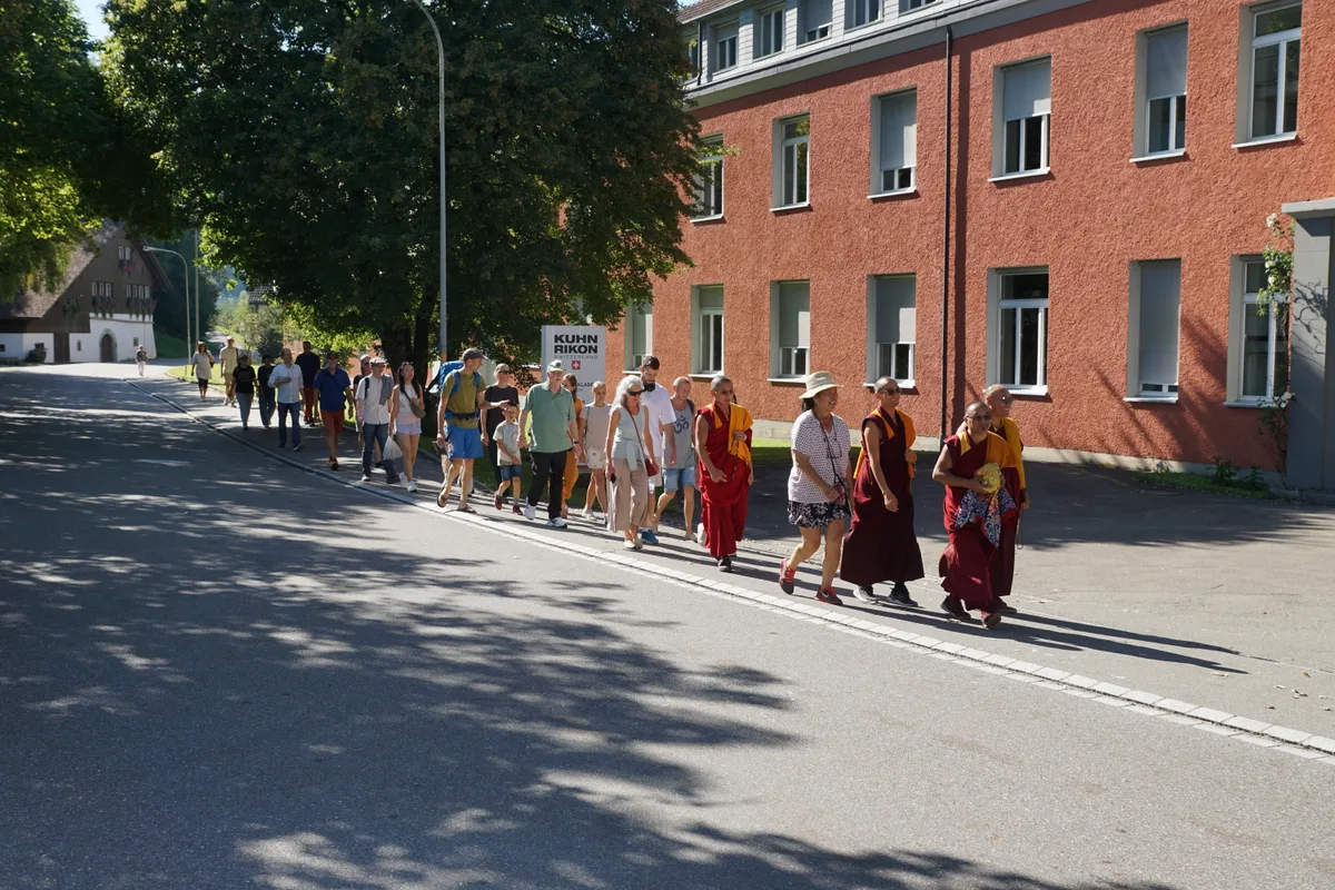 Man sieht eine Menschengruppe mit buddhistischen Mönchen bei Kuhn Rikon vorbeigehen.