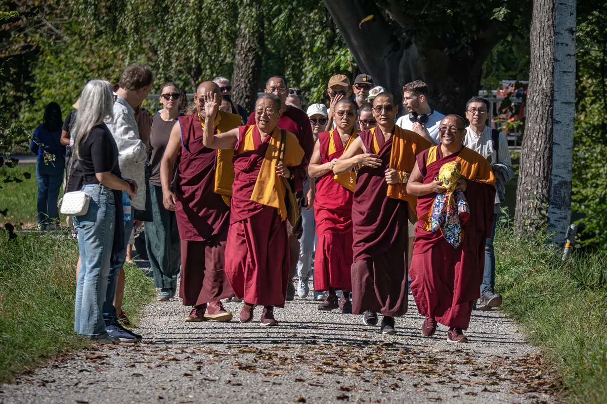 Am Ufer der Töss wird die fröhliche Prozession schon von weiteren Interessierten erwartet. Man sieht buddhistische Mönche, die fröhlich anderen Leuten zuwinken.