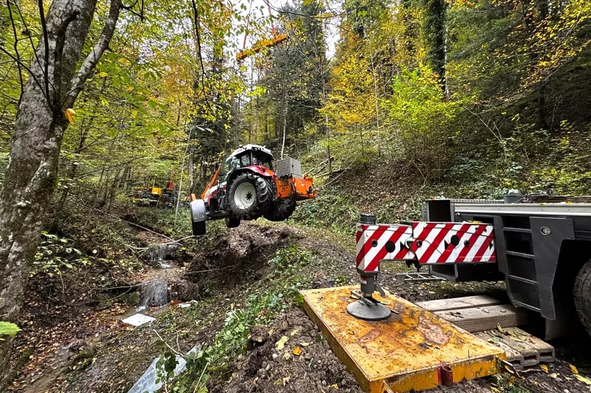 Dann war ein Kran nötig, um den Traktor behutsam aus dem Bach herauszuheben. Ein Kran hebt einen Traktor aus einem Bach.