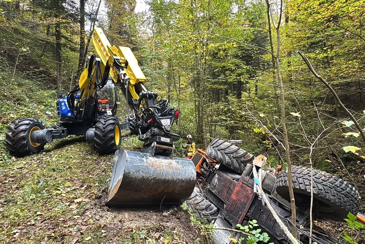Wie nur kriegt man einen tonnenschweren Traktor aus einem Bach? Eine Herausforderung für die Einsatzkräfte. Ein umgekippter Traktor liegt rechts in einem Bach. Links auf einem Waldweg steht ein zweites Gefährt.
