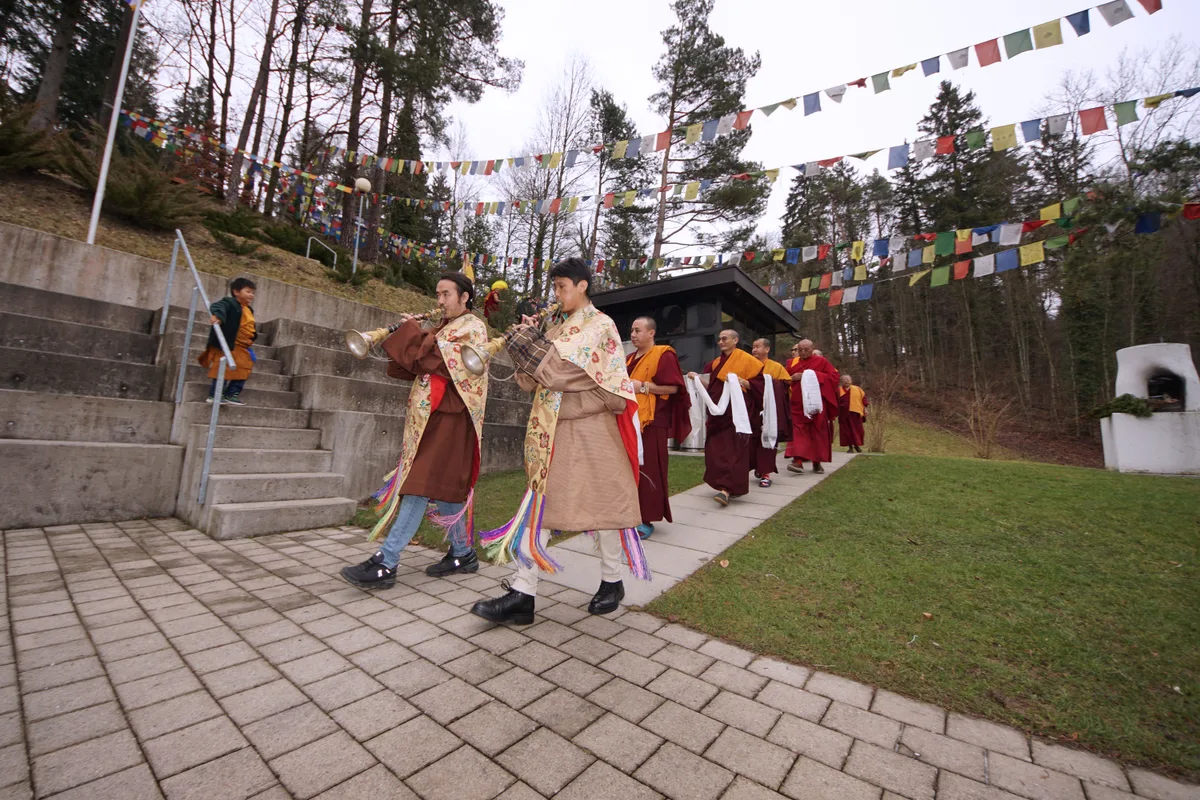 Man sieht tibetische Mönche, die von Trompetern begleitet werden.