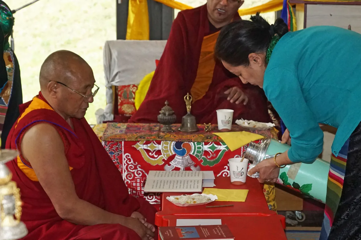 Man sieht, wie ein Mönch eine Tasse Tee bekommt.