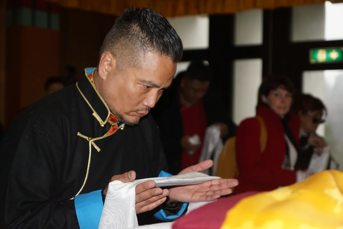 Man sieht einen tibetischen Mann, der sich mit einer Glücksschleife verneigt.