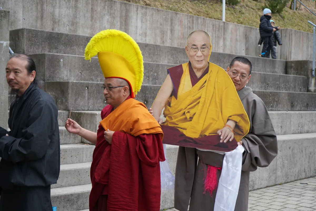 Man sieht tibetische Mönche, die eine Ikone des Dalai Lama tragen.