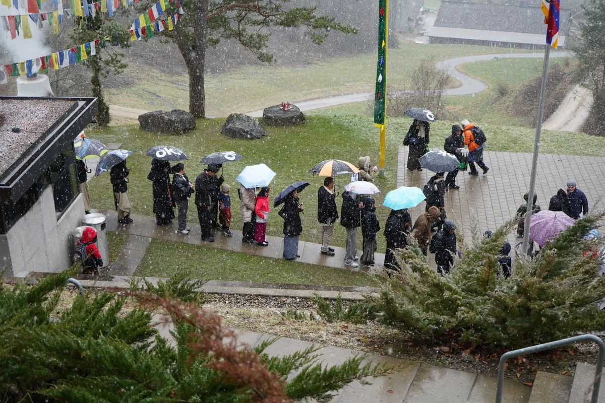 Man sieht Menschen bei Schneeregen in der Schlange stehen.