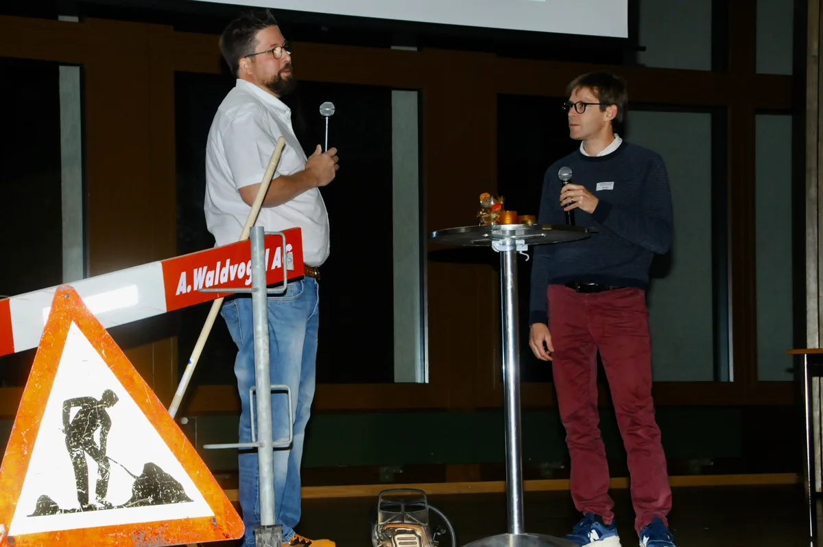 Man sieht zwei Männer an einem Podiumsgespräch.