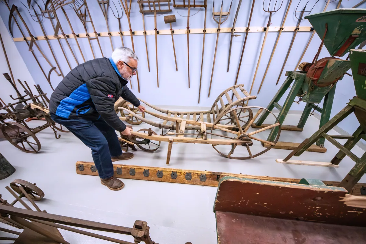 Fritz Fuhrimann zeigt, wie aufwendig früher die Feldarbeit von Hand war. Fritz Fuhrimann hält eine Landmaschine.