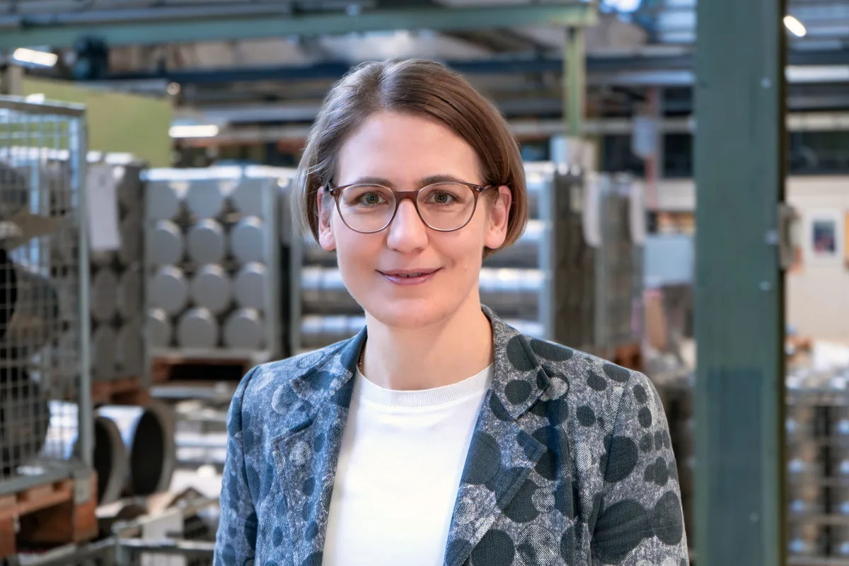 «Ich empfinde es als Privileg, auf eine solche Firmengeschichte zurückzublicken»: Dorothee Auwärter, VR-Präsidentin von Kuhn Rikon. Eine Frau mit Brille, hellem Shirt und dunkel gemustertem Blazer. Sie steht in einer Fabrikhalle.