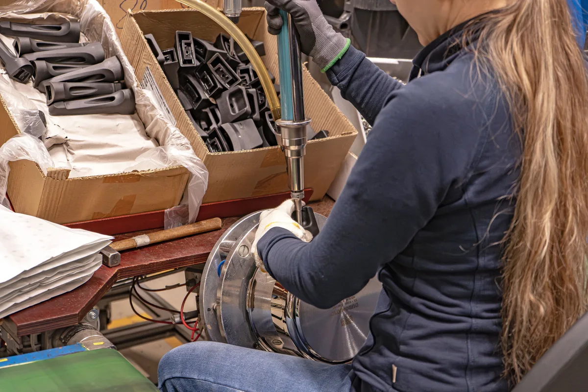 Von den 260 Mitarbeitenden sind rund 190 in der Schweiz beschäftigt. Blick in die Produktion von Kuhn Rikon am Hauptsitz in Rikon. Rohlinge von Töpfen. Eine Mitarbeiterin montiert Griffe an einen Topf.