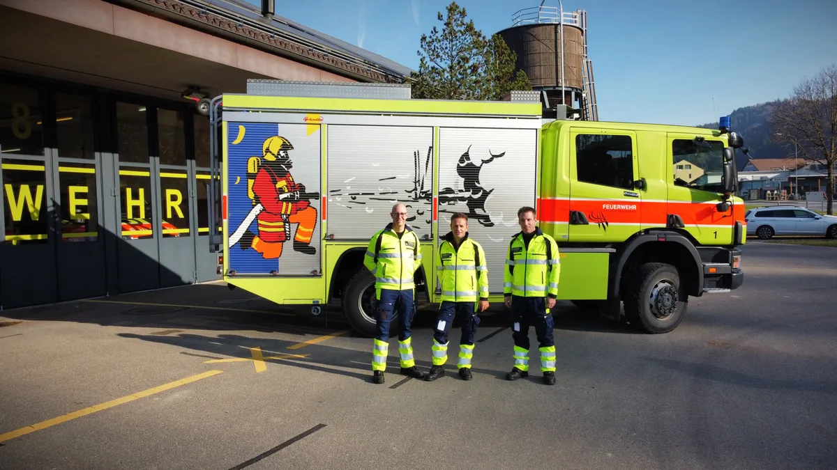 Drei Feuerwehrleute vor einem Tanklöschfahrzeug.