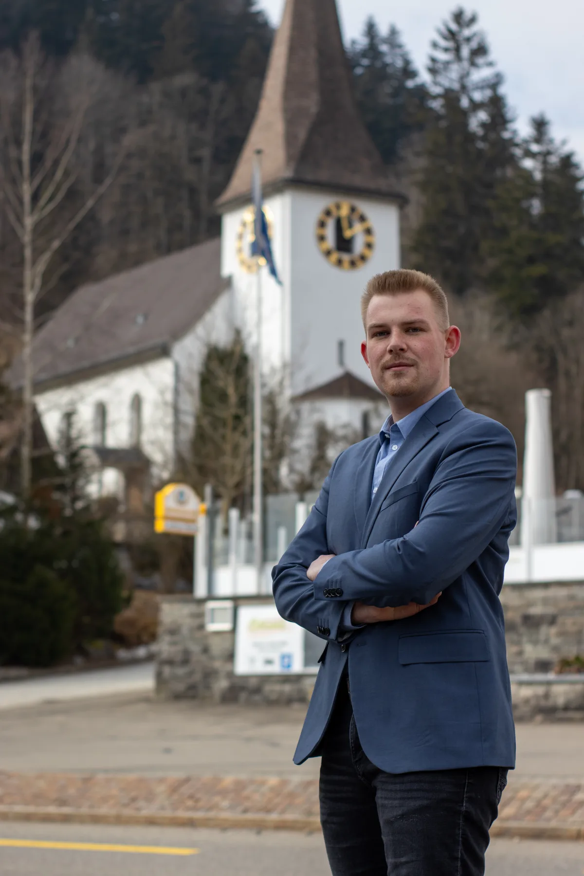 Man sieht einen Mann, der mit verschränkten Armen in einem Dorf posiert.