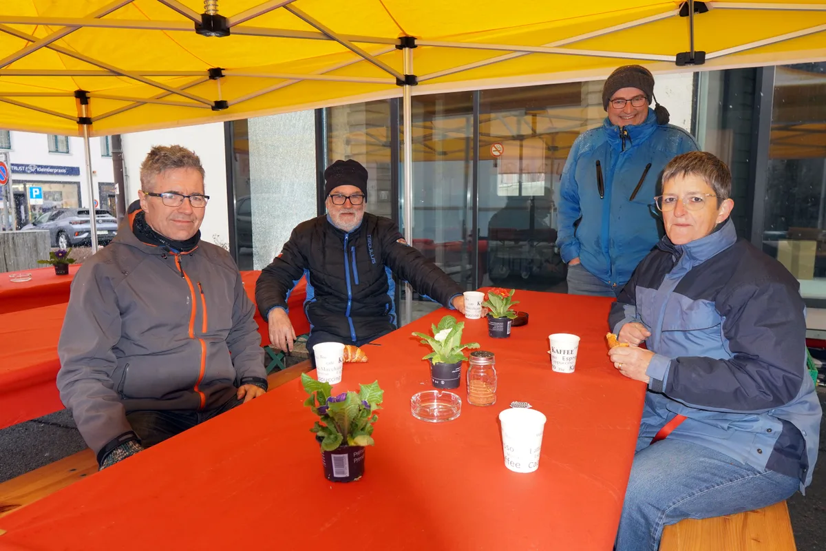 Man sieht vier Menschen an einer Festbank sitzen. 