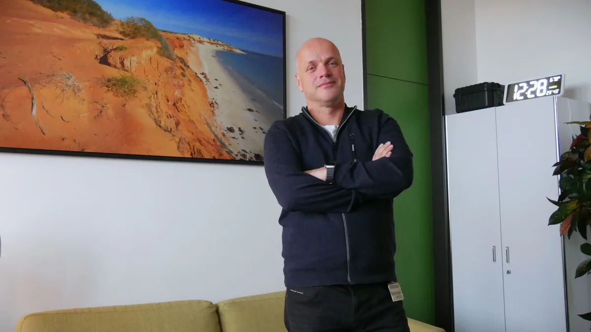 Man sieht einen Mann in Sweatjacke und Jeans, der die Arme verschränkt.