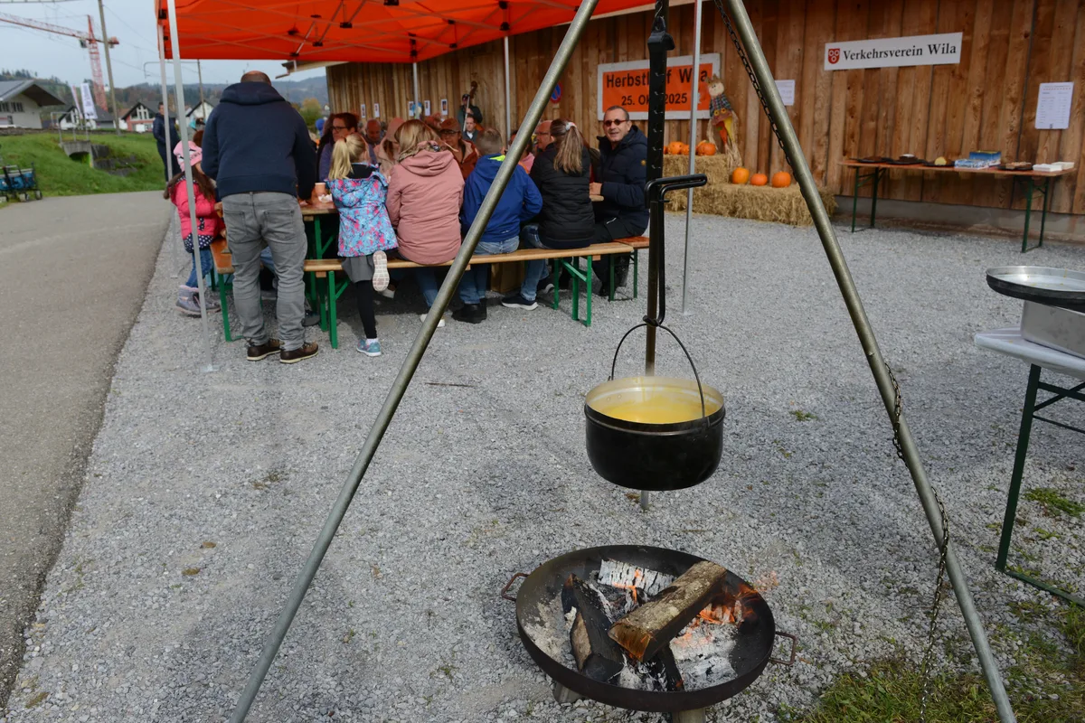 Man sieht einen Topf mit Kürbissuppe, der über einem offenen Feuer hängt.