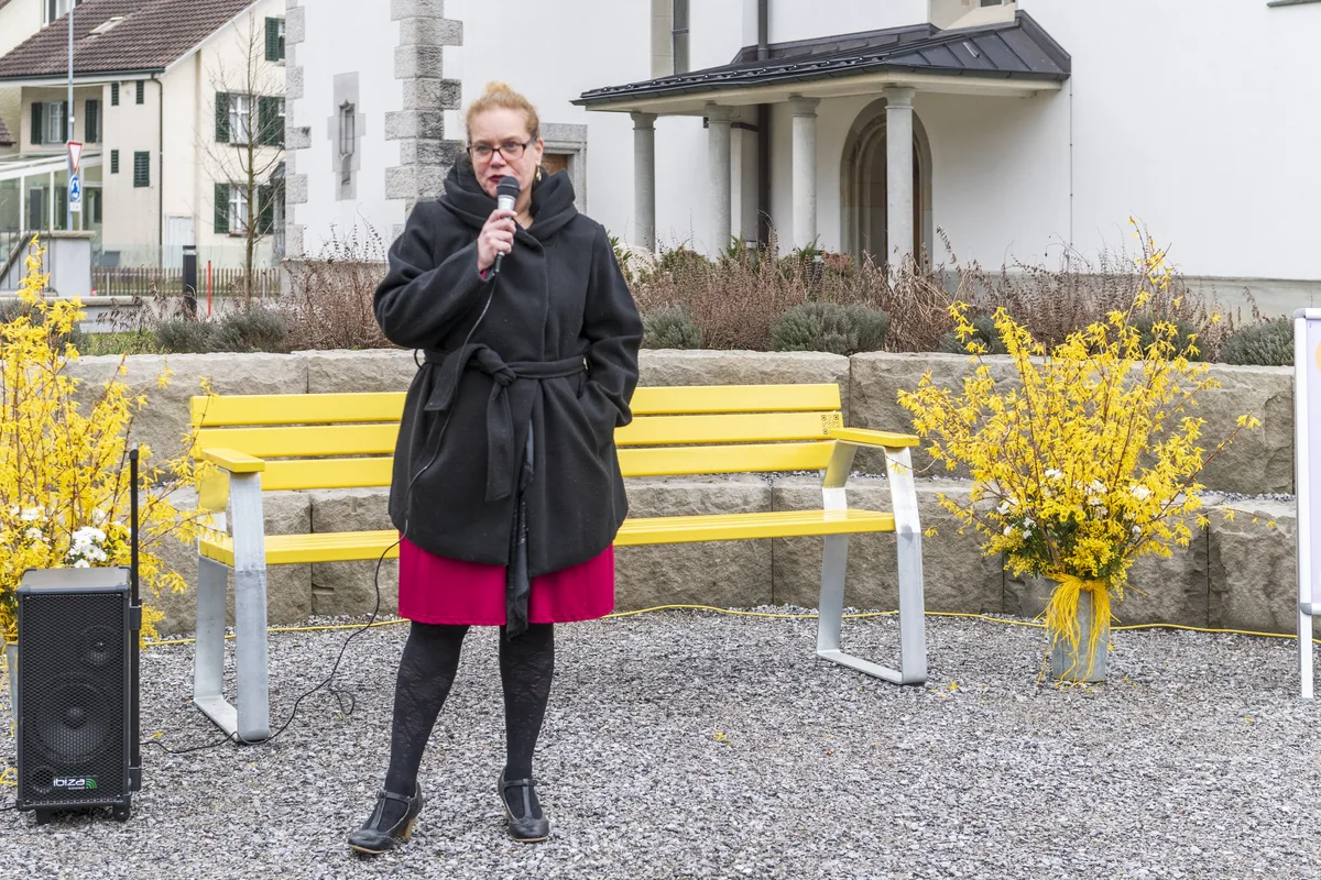 Platz findet das Bänkli im Kirchenpark. Für Monika Di Benedetto, die Präsidentin der Kirchenpflege, ist das der richtige Ort. Frau vor gelber Sitzbank