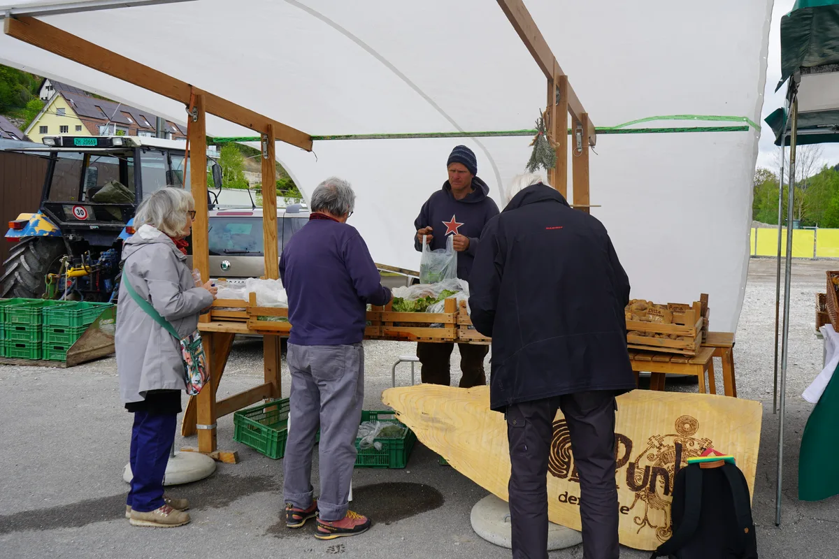 Man sieht Personen, die an einem Marktstand einkaufen.