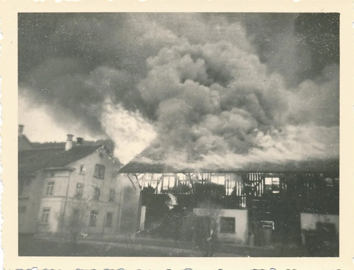 Im ehemaligen Ökonomiegebäude wurde unter anderem Baumwolle gelagert. Man sieht ein Haus, das in Flammen steht auf einem Schwarzweissfoto.