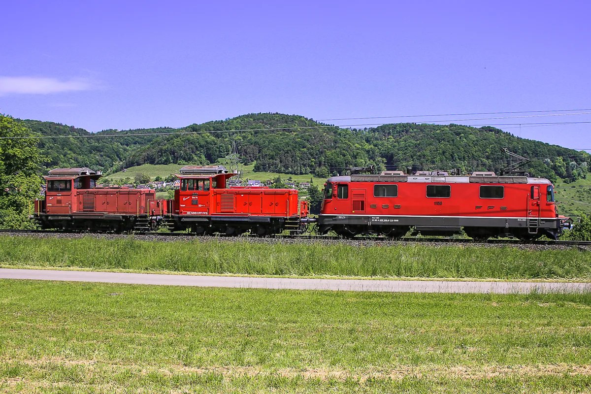 Man sieht eine Elektrolok, die zwei Dieselloks zieht.