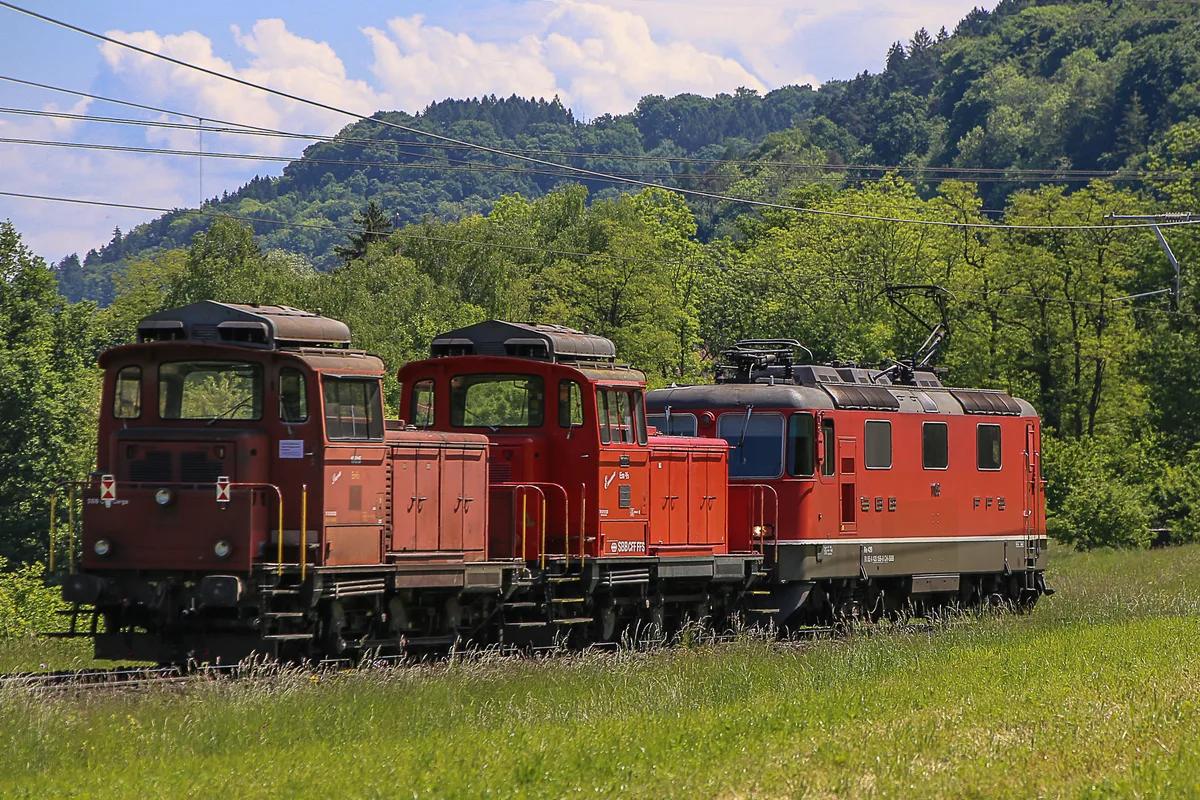 Man sieht eine Elektrolok, die zwei Dieselloks zieht.
