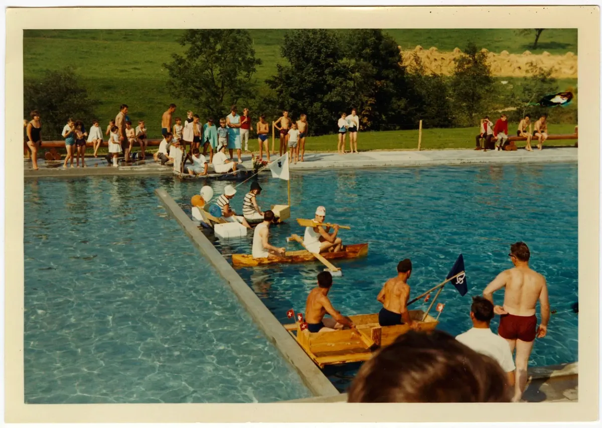 Man sieht ein altes Foto eines Bootsrennens in einem Schwimmbad.