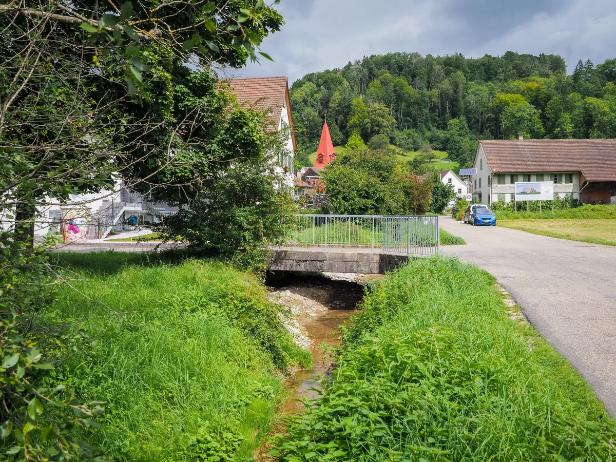 Man sieht einen kleinen Bach und ein Dorf im Hintergrund.