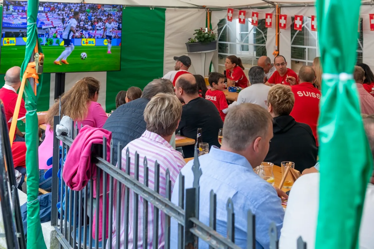 Menschen sitzen an Tischen während Fussball läuft.