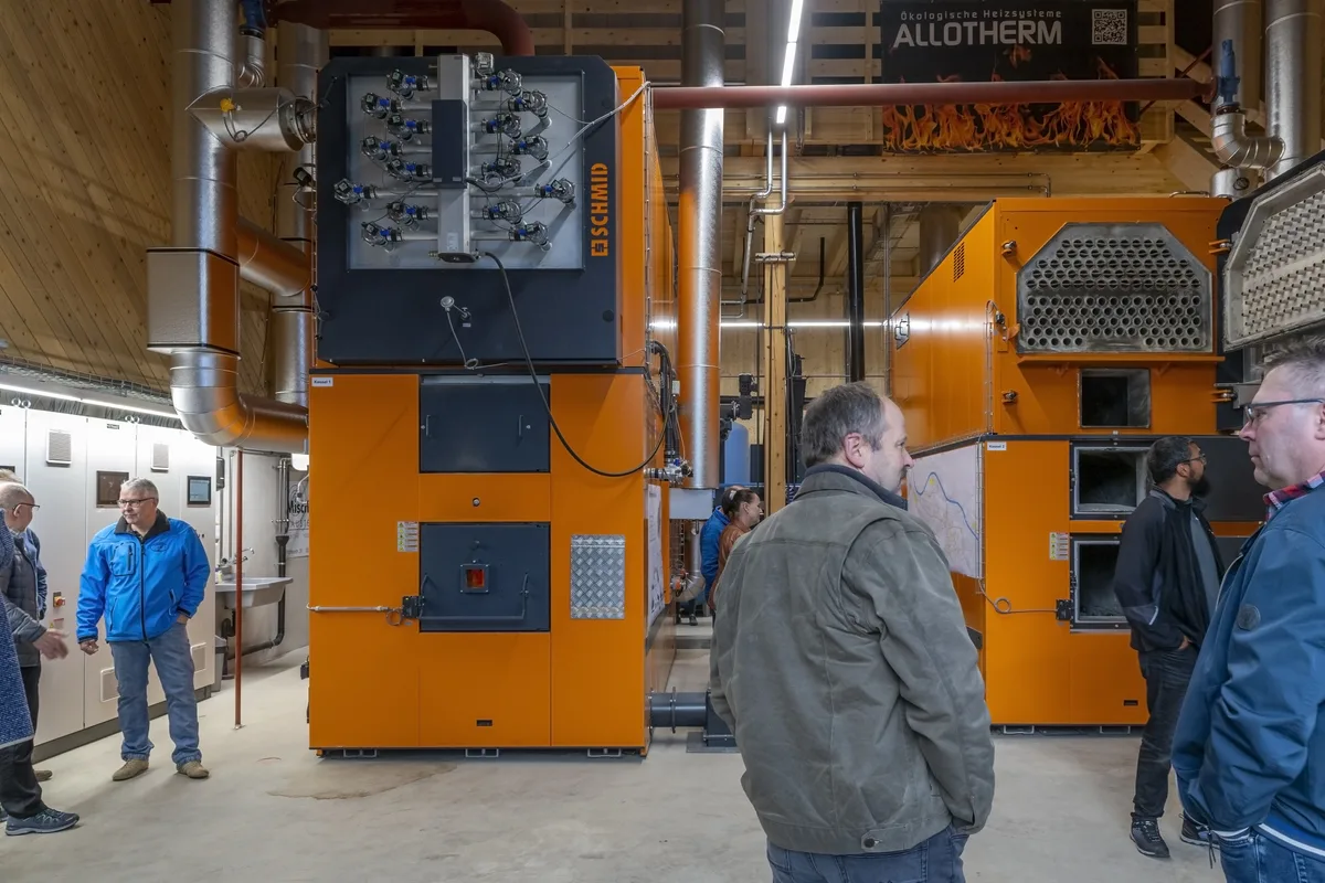 Viel Technik im Innenraum zieht die Aufmerksamkeit der Besucher auf sich. Orange Öfen und Menschen, die rundherum stehen.