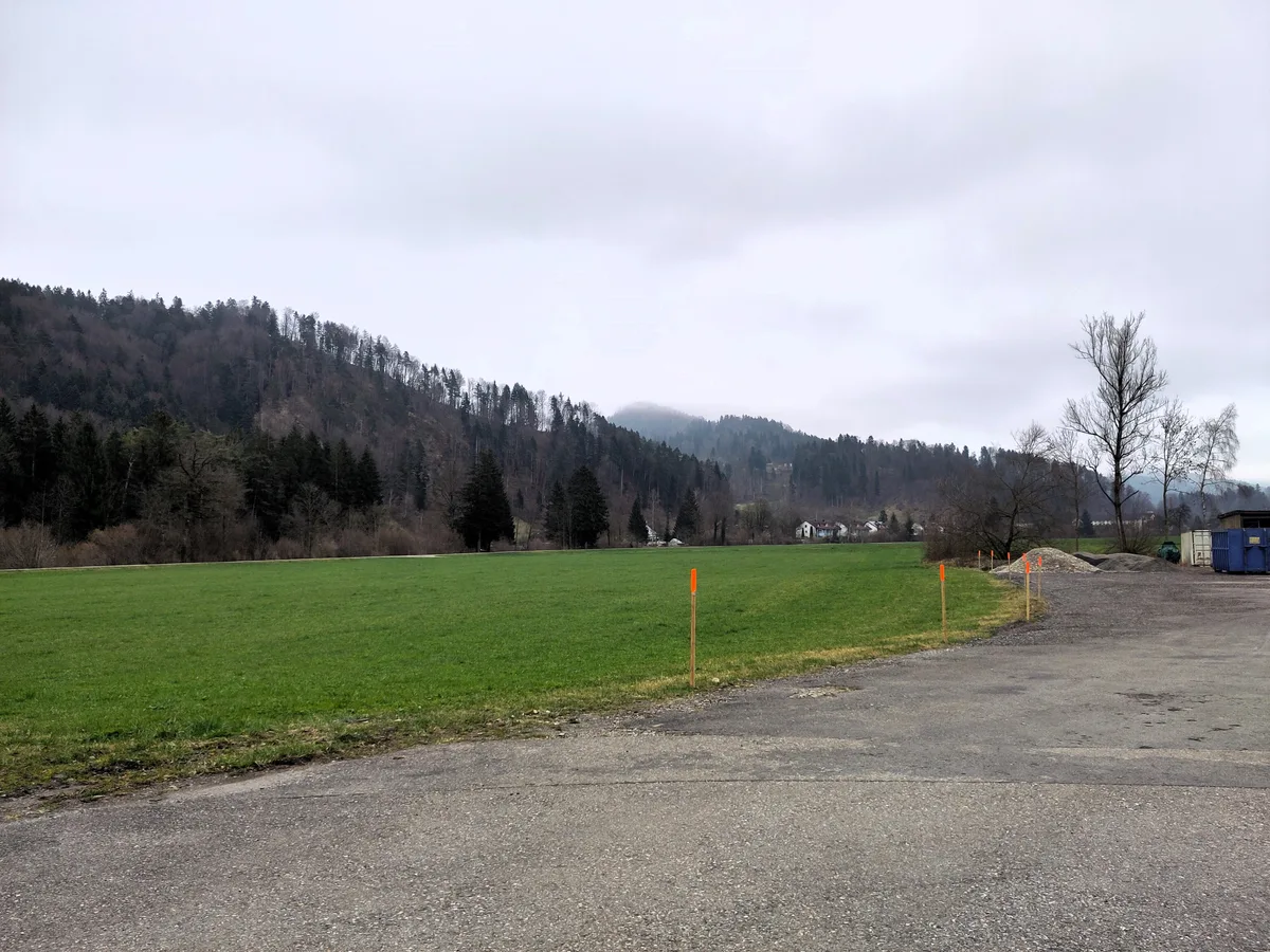 Man sieht einen Kiesplatz und eine Wiese.