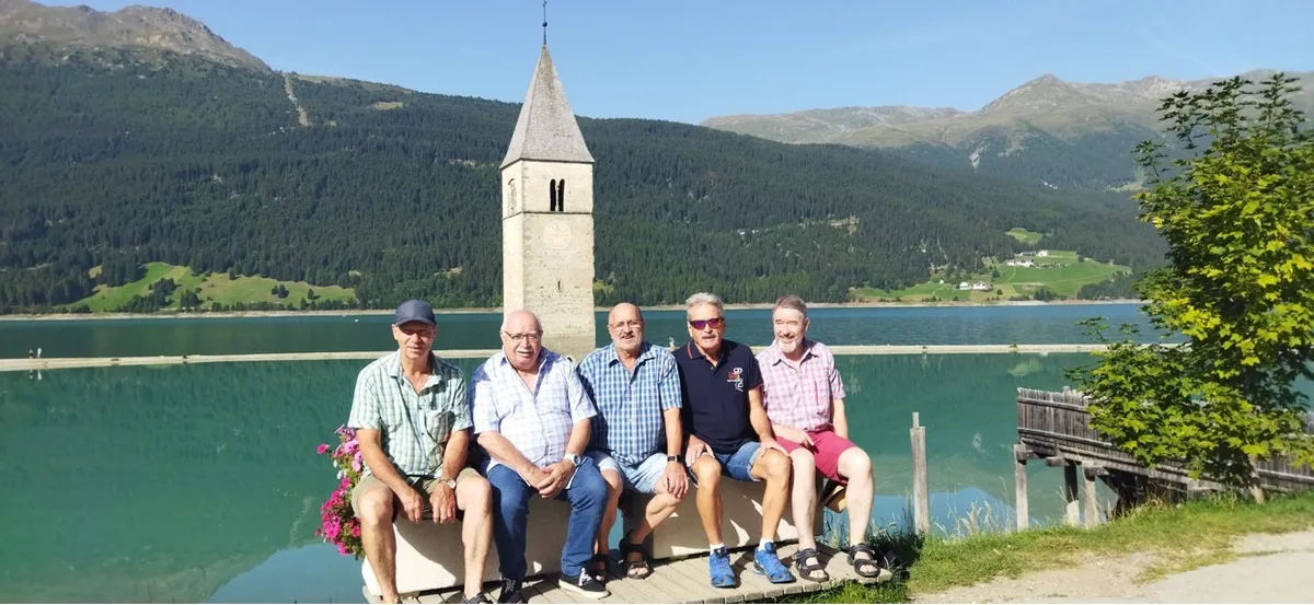 Die letzte Jassreise führte nach Resch in Italien. Man sieht fünf Männer vor einem Turm, der in einem See steht.