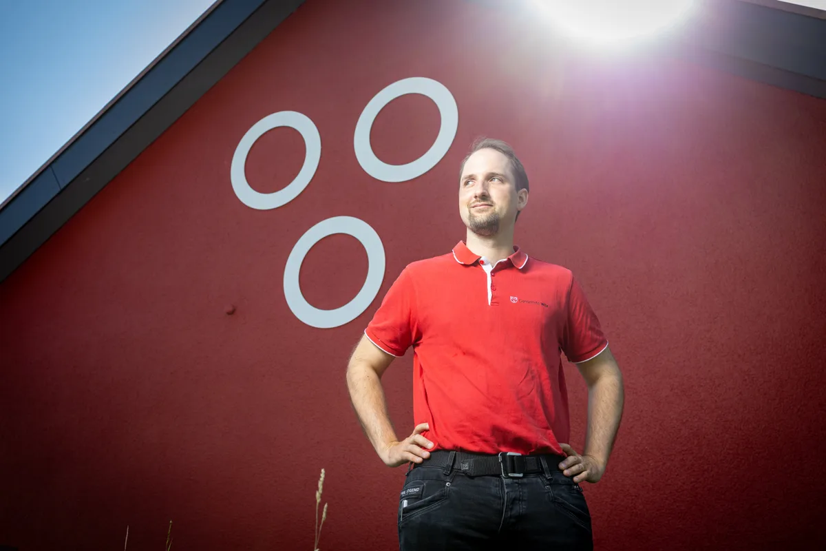 Simon Mösch vor dem  Man sieht einen Mann vor einer roten Wand.