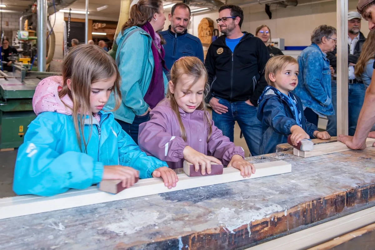 Marina, Jasmin und Philipp schleifen an ihren eigenen Stelzen. Damit es dann zu Hause kein Durcheinander gibt, werden diese im nächsten Arbeitsschritt mit einer persönlichen Lasergravur versehen. Grosser Besucherandrang in der Schreinerei Furrer in Wila.