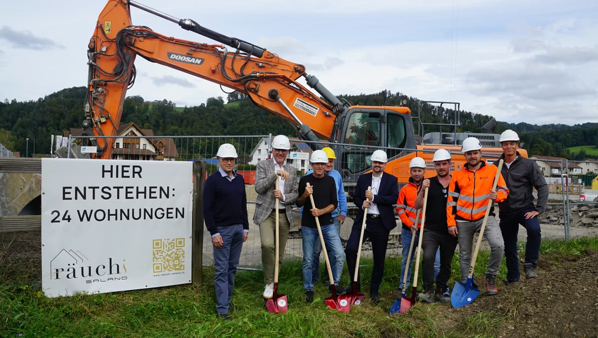 Man sieht Herren mit Bauhelmen und Schaufeln vor einem Bagger.