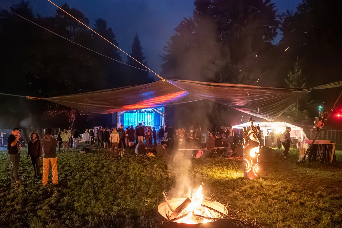 Man sieht Menschen an einem Festival. Es ist dunkel, und es brennen Feuerschalen.