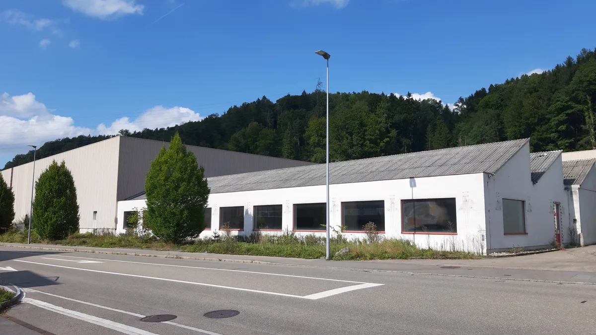 Man sieht eine ältere und eine neuere Fabrikhalle an einer Strasse.