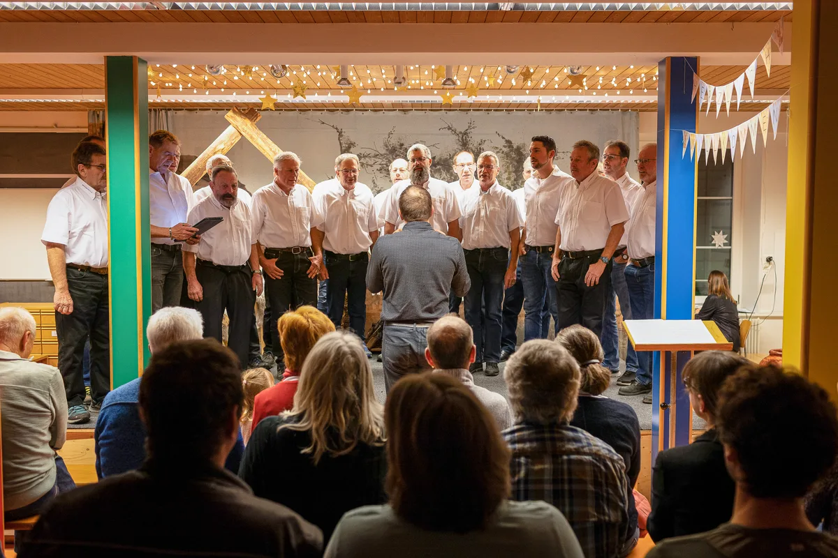 Der Männerchor stimmt das Publikum auf das Theater ein. Man sieht einen Männerchor, der auf der Bühne steht. Alle singen.