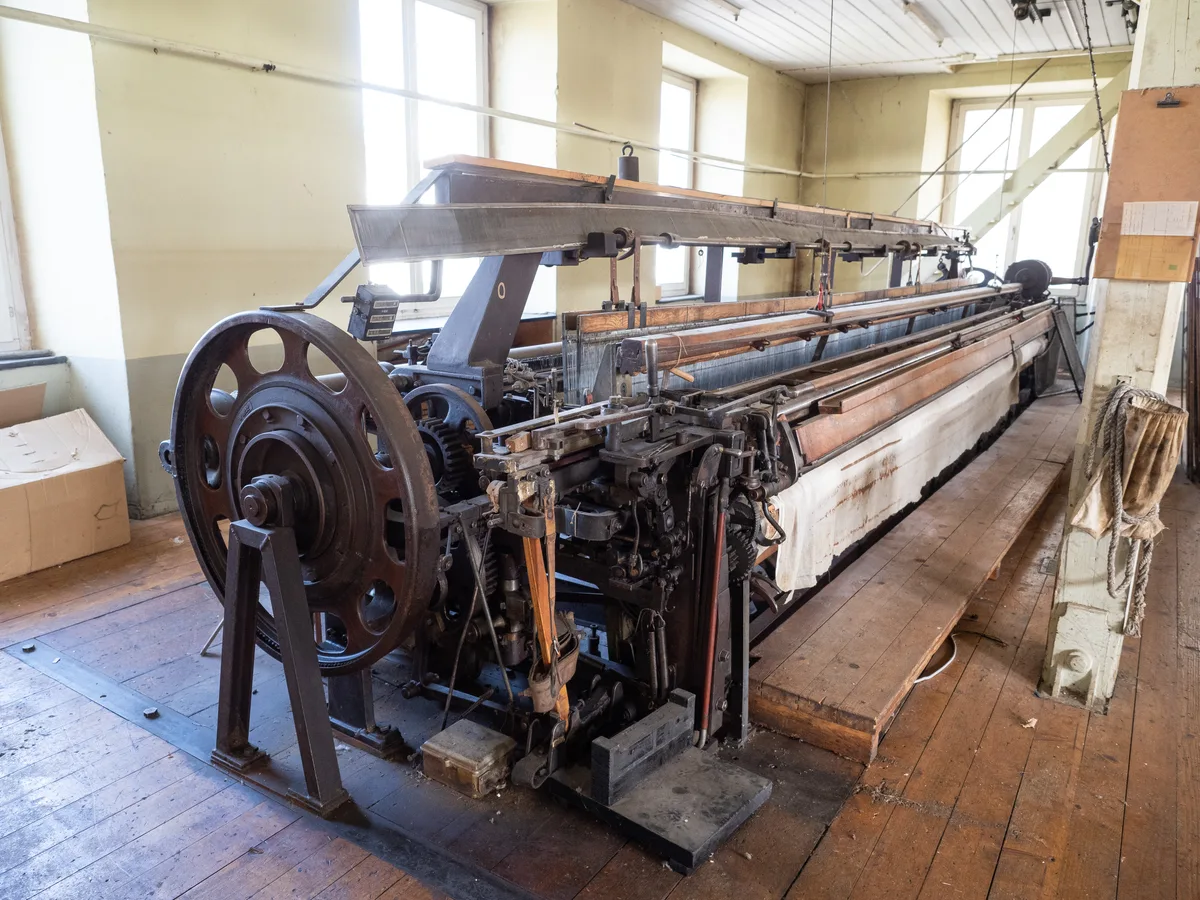 In der alten Produktionshalle stehen noch die alten Maschinen für das Breitgewebe. In einigen Jahren findet man hier Wohnungen. Man sieht eine alte Webereimaschine.