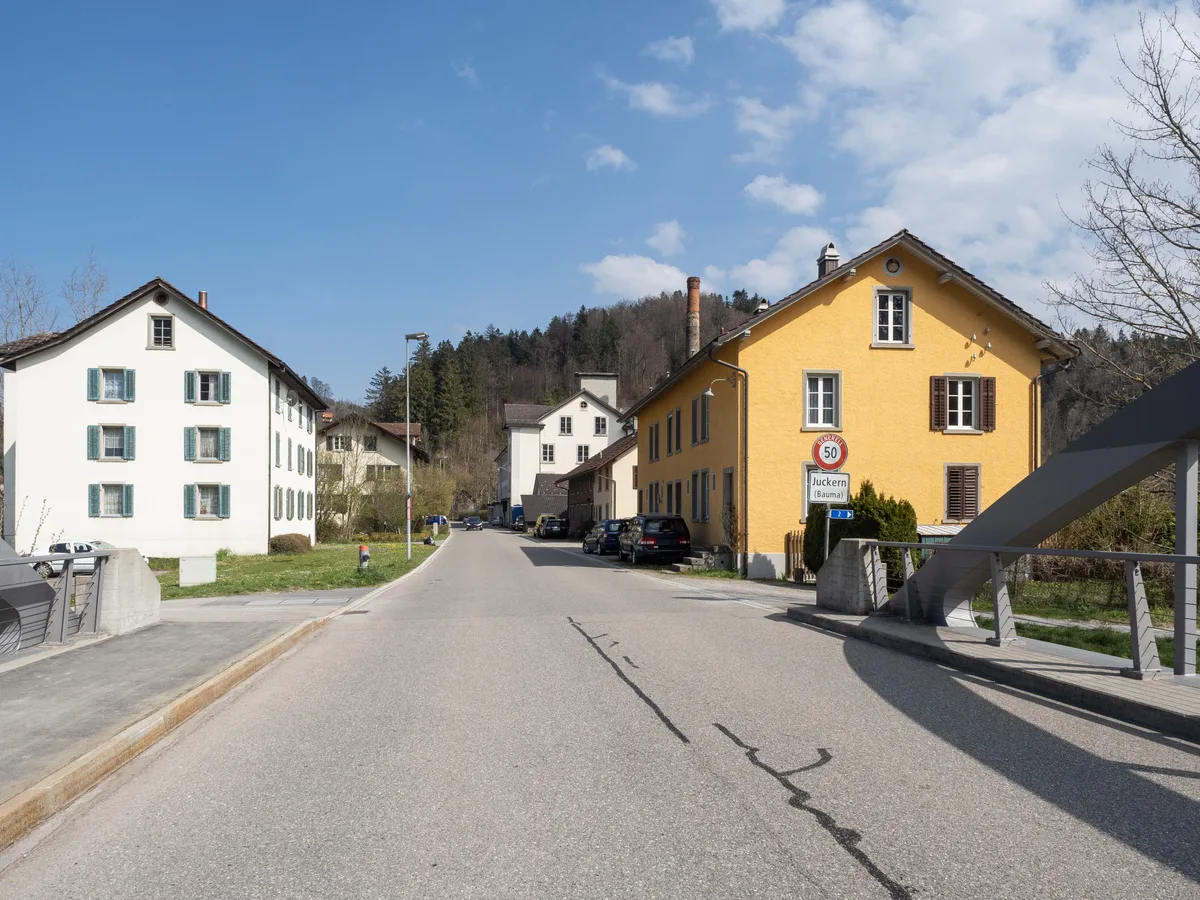 Die zahlreichen Gebäude rund um die alte Weberei werden meist umgebaut.  Man sieht den Eingang von Juckern mit Häusern und dem Hochkamin.