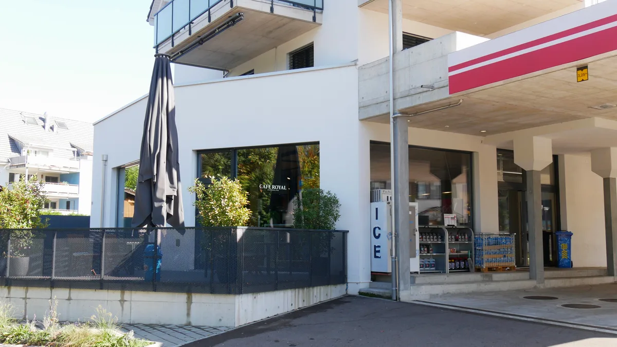 Man sieht einen Balkon mit Sitzplätzen, der Teil eines Tankstellenshops ist.