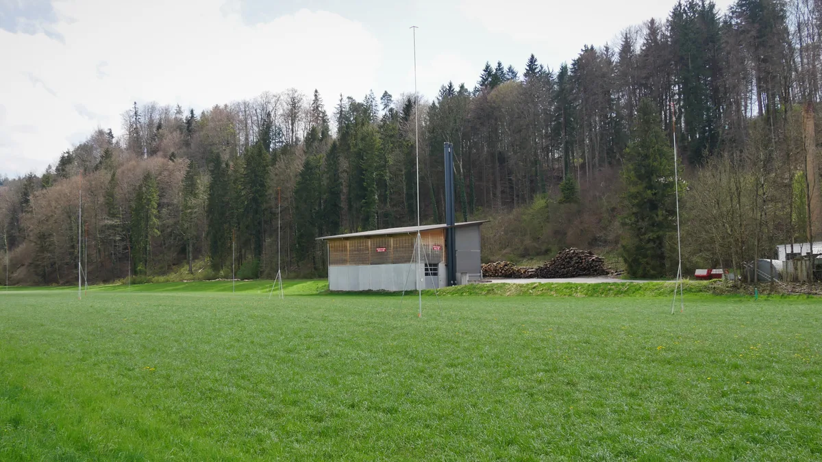 Man sieht Bauvisiere auf einer Wiese. Im Hintergrund sieht man einen Wald und Wohnhäuser.