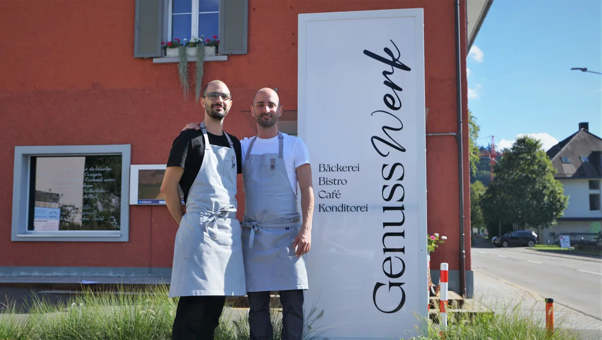 Foto von zwei Männern mit grauer Schürze und Glatze vor einem Verkaufslokal.