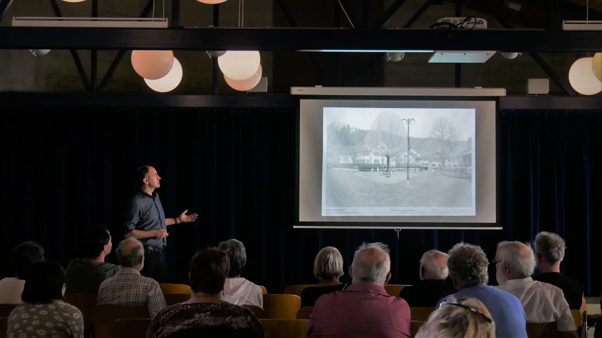 Ein Mann mit anthrazitfarbenem Hemd hält einen Vortrag vor Publikum.