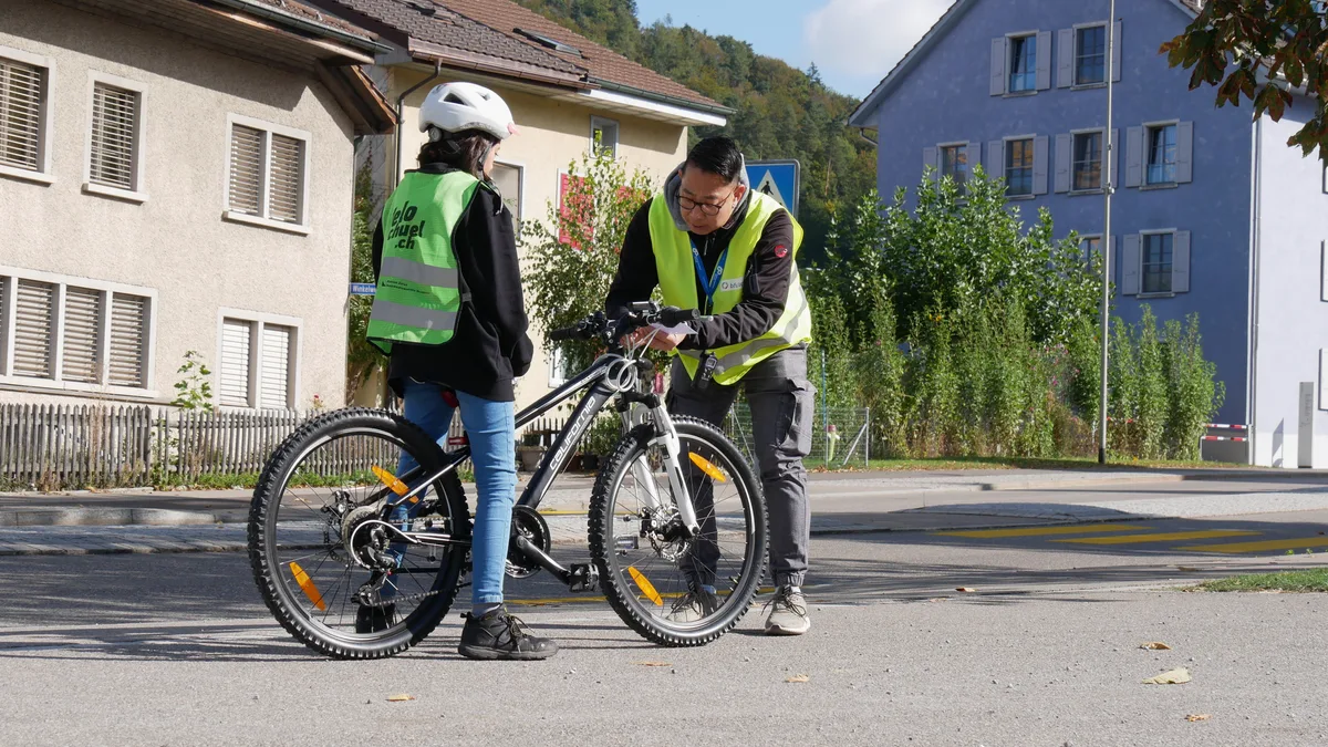 Ein Herr spricht mit einem Kind auf einem Velo.