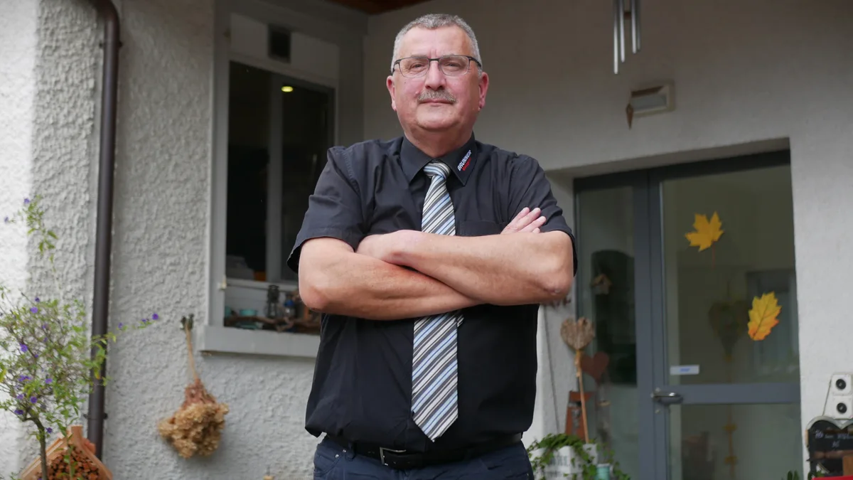 Man sieht einen Mann mit Hemd und Krawatte, der seine Arme verschränkt.