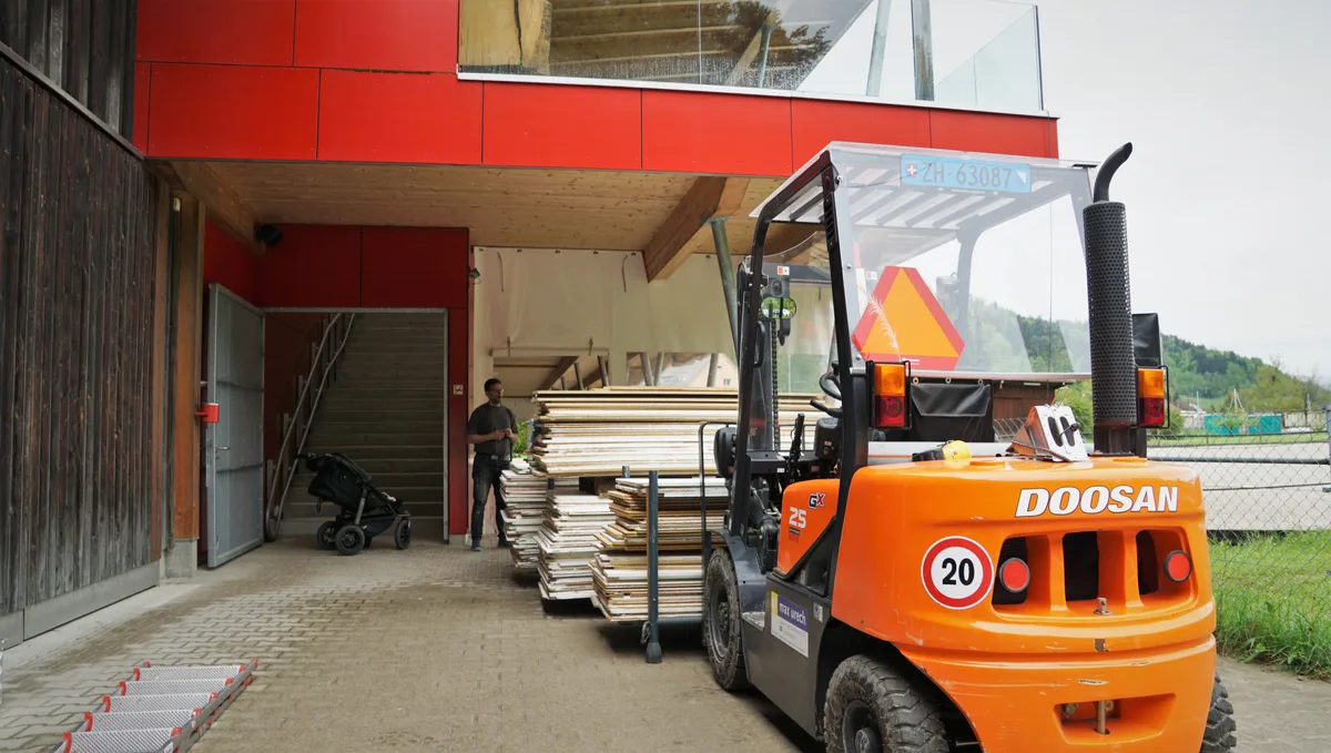 Man sieht einen orangenen Gabelstapler, der Holzlatten aufgeladen hat.