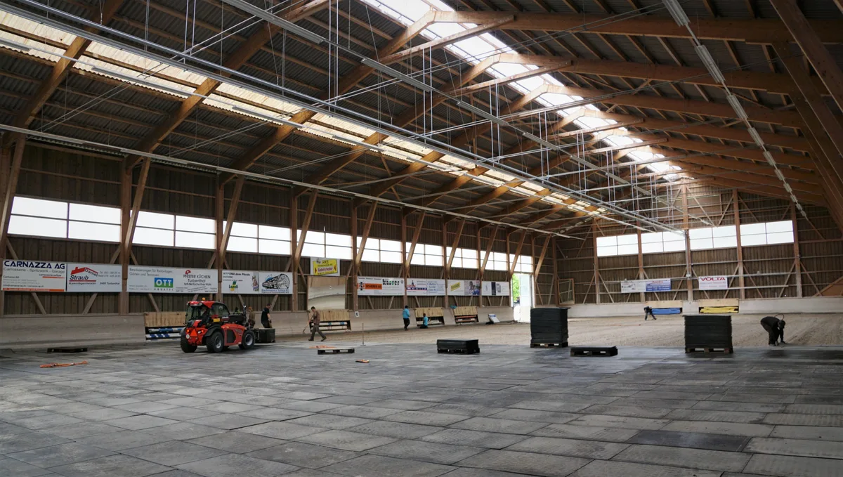 Man sieht Helfer, die den Boden in einer Halle verlegen.